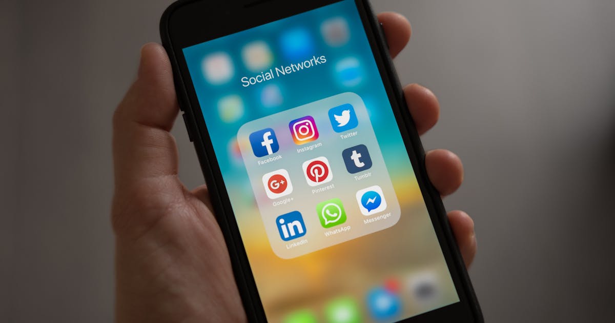 Person holding iPhone showing social media apps including Facebook and Instagram